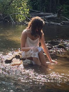 a woman sitting on rocks in the middle of a river with flowers floating all over her