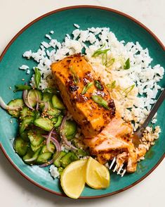 a green plate topped with salmon and rice next to a side of cucumbers