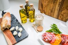 bread, tomatoes and other food items on a cutting board next to olive oil bottles