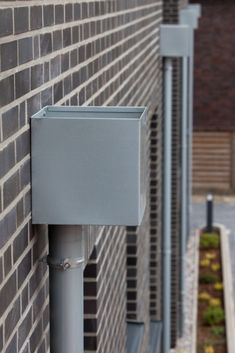 the corner of a brick building with a metal pole and square box on it's side