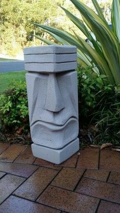 a cement sculpture sitting on top of a brick walkway next to plants and trees in the background