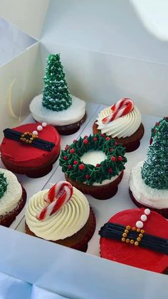 twelve decorated christmas cupcakes in a box with white frosting and red icing