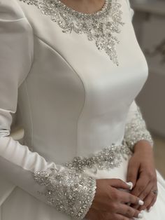 a woman in a white wedding dress with silver beading on her sleeves and arms