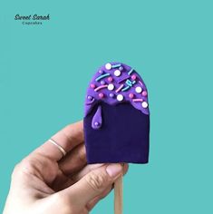 a hand holding a purple cupcake with sprinkles on it