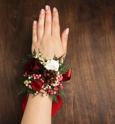 a woman's hand wearing a red and white wrist corsage on top of a wooden table