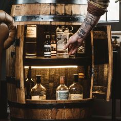 a man is reaching into a wooden barrel with alcohol bottles on the bottom and inside