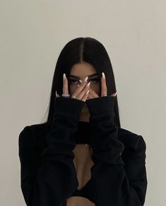 a woman covering her face with both hands while standing in front of a white wall