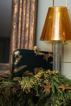 a gold lamp is next to a green christmas garland and a black purse on a table