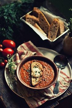 a bowl of soup on a plate with bread and tomatoes next to it, along with other food items