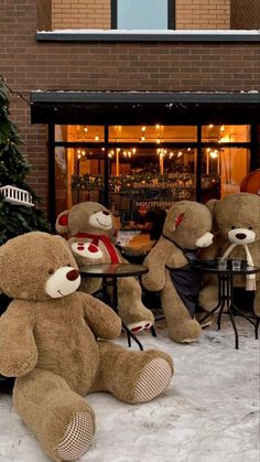 three teddy bears sitting at a table outside in the snow