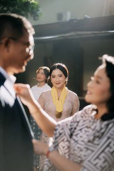 two women and one man are standing in front of each other with yellow necklaces on