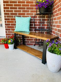 a wooden bench sitting in front of a brick wall next to potted plants and flowers