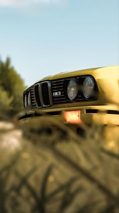 the front end of a yellow car driving down a road