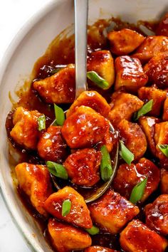 a bowl filled with chicken and sauce on top of a white countertop next to a silver spoon