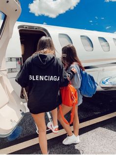 two girls are getting off an airplane with their back to the camera and one girl is holding onto her backpack