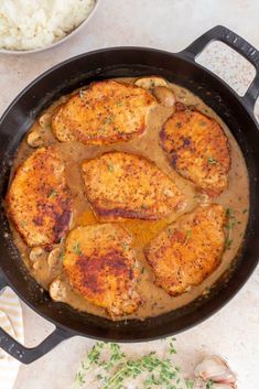 chicken with gravy in a skillet next to white rice and parsley