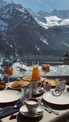 a table with plates and cups on top of it in front of snow covered mountains