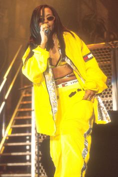 a man in yellow outfit holding a microphone and singing into a mic on stage with stairs behind him