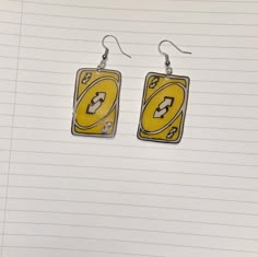 pair of yellow and black earrings with lightning bolt design on them, sitting on top of lined notebook paper