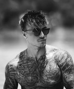 a man with tattoos on his chest wearing sunglasses and looking off to the side in black and white