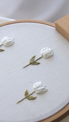 three white flowers sitting on top of a table next to a piece of wood and thread