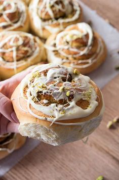 a person is holding a pastry with white icing on it and other pastries in the background