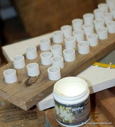 several white cups sitting on top of a wooden table next to a jar of paint