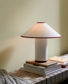 a lamp sitting on top of a table next to some books and a bed sheet