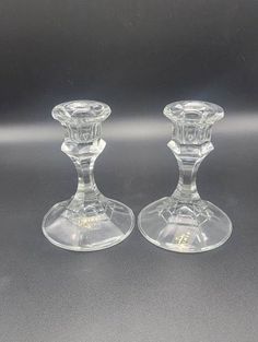 two clear glass candlesticks sitting side by side on a gray surface with one candle in the middle