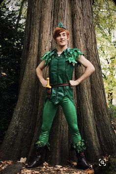 a man dressed as peter panton standing in front of a tree with his hands on his hips