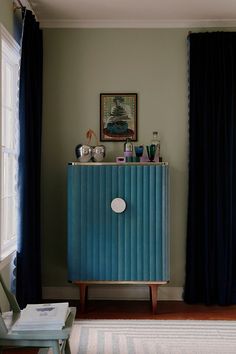 a blue cabinet in the corner of a room next to a window with black curtains