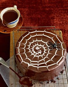 a spider web cake with chocolate frosting on a cooling rack next to a cup of coffee