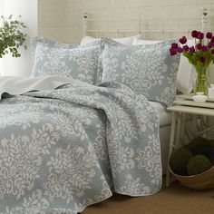 a bed with a blue and white comforter next to a plant in a vase