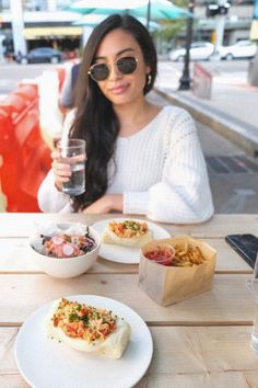 a woman sitting at a table with plates of food and drinks in front of her