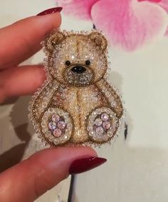 a teddy bear brooch is being held by a woman's hand in front of a pink flower