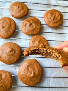 a person holding a cookie in front of some cookies on a cooling rack with one bite taken out