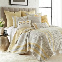 a bed with yellow and white comforters, pillows and blankets on top of it