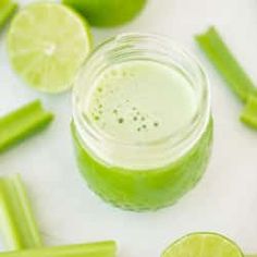 a jar filled with green liquid next to sliced celery and limes on a white surface