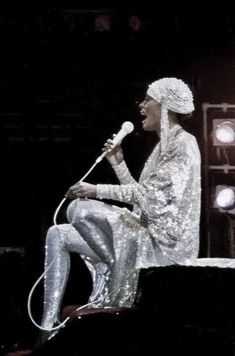 a woman sitting on top of a stage while holding a microphone