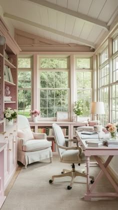 a home office with pink walls and white furniture in front of two large windows that look out onto the woods