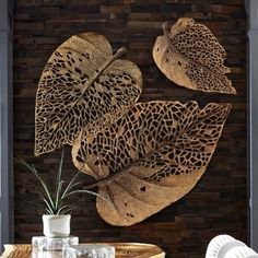 three decorative leaf shaped wall hangings in front of a wooden wall with a vase and plant