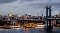 the city skyline is lit up at night as seen from across the water with a bridge in the foreground