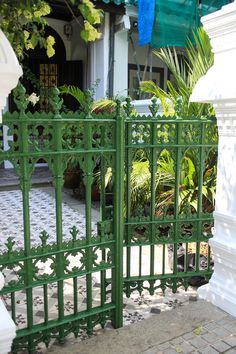 a green gate is open on the side of a building with potted plants behind it