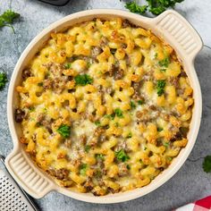 a casserole dish with sausage and cheese in it on a gray surface next to some parsley