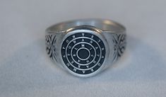 This ring was designed with the Disc of King Solomon Tetragrammaton.  The beautiful pewter ring is a silver color and the background is blackened to bring out the fine detail of the design. Our rings are 100% Lead and nickel free pewter and made in the USA The dragon design part of the ring measures about 15 mm tall and wide or over 1/2 inch The ring band tapers from about 15mm to about 4.5mm at the bottom and is about 1.75mm thick We offer free shipping within the USA Rings are available in sizes 7 to 14 Spiritual Round Signet Ring With Polished Finish, Seal Of Solomon Ring, Spiritual Sterling Silver Ring With Cabochon, Solomon’s Seal, Adjustable Moon-shaped Spiritual Ring, Solomons Ring, Seal Of Solomon, Pewter Ring, King Solomon