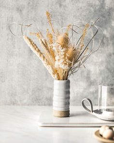 a vase filled with dried flowers on top of a table next to a coffee cup