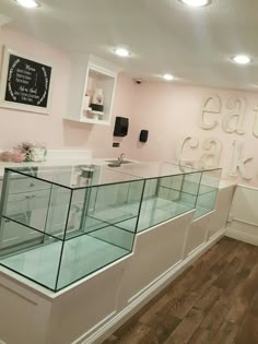 an empty glass counter in a bakery with white lettering on the wall and wood flooring