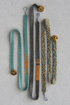 four beaded bracelets are lined up on a white surface, one is gold and the other two are blue