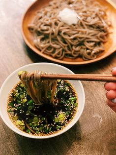 a person holding chopsticks over a bowl of noodles