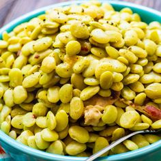 a blue bowl filled with green beans on top of a wooden table next to a spoon